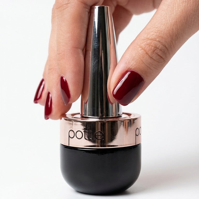 Hand holding a black and rose gold pottle nail bottle on a white background