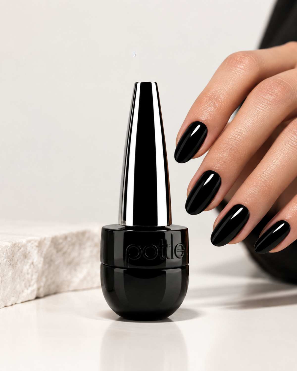 A bottle of glossy black nail polish with a metallic silver cap stands on a white surface next to a hand with matching black manicured nails. The brand name 'potte' is embossed on the bottle.